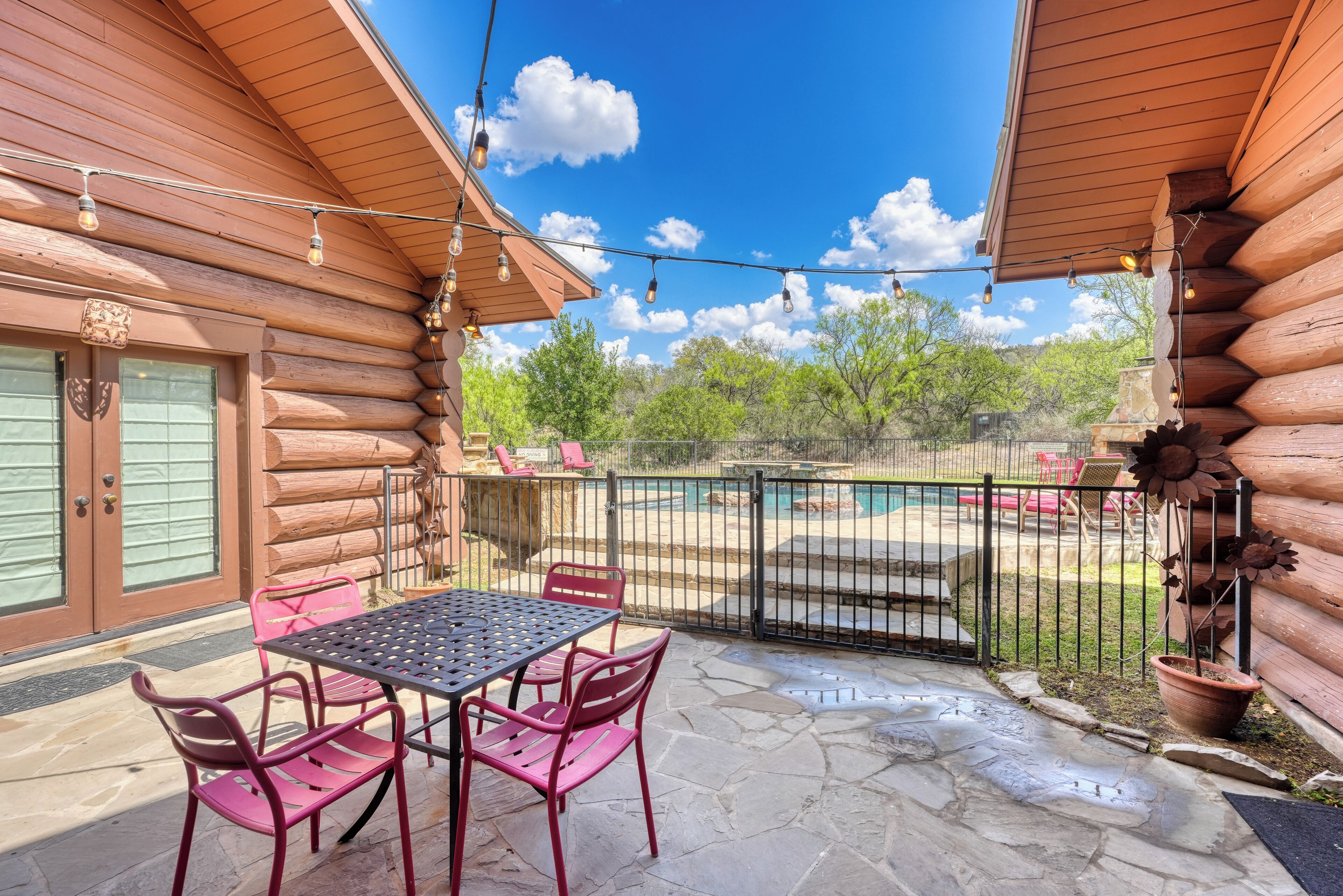 Une cabane en rondins dotée d’un patio avec une table et des chaises en pierre, une piscine et un espace clos délimité par une clôture.