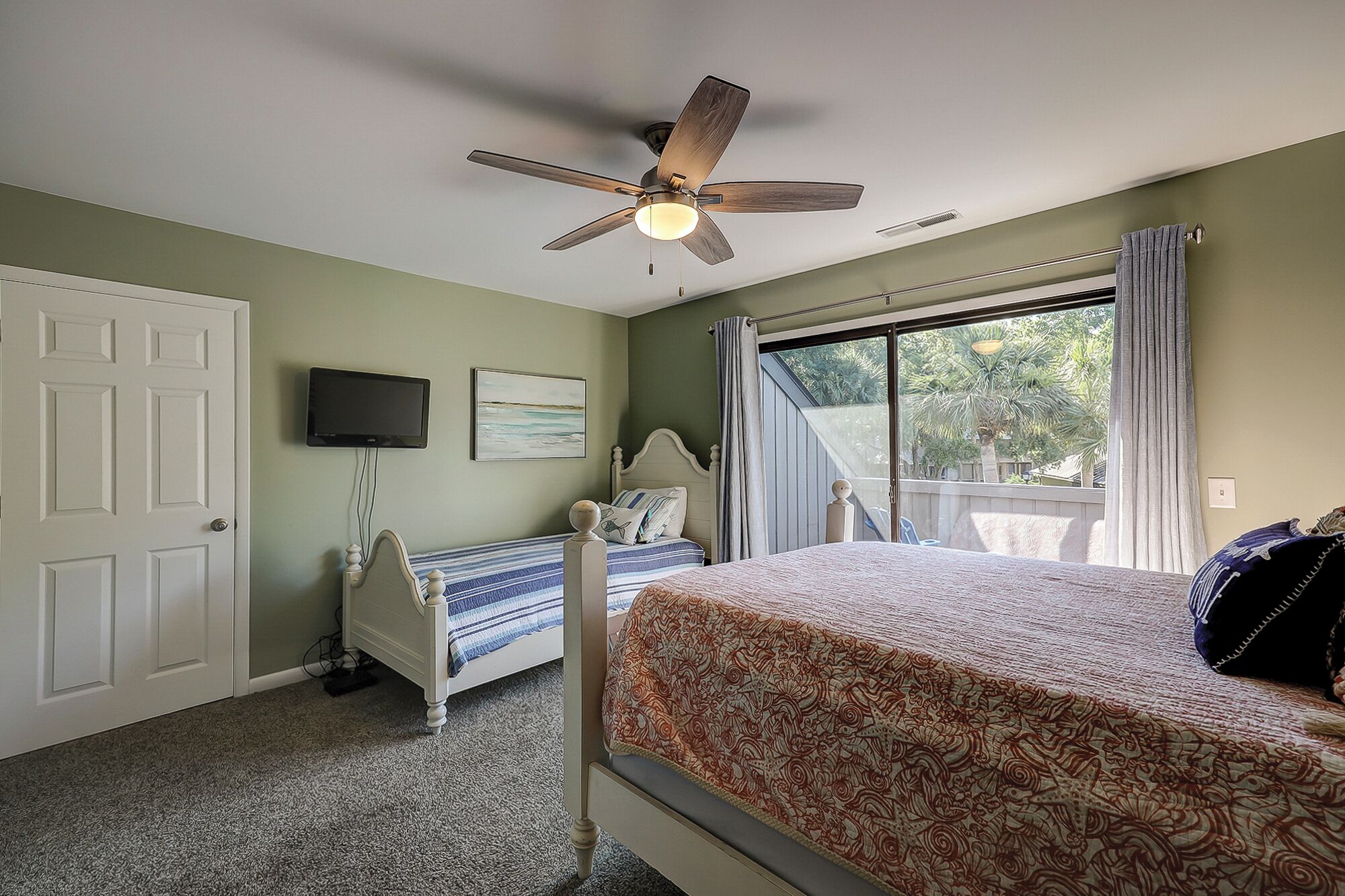 Une chambre à coucher avec un lit, un ventilateur de plafond, une télévision et une fenêtre avec des rideaux.