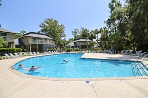 A swimming pool with lounge chairs and umbrellas, surrounded by buildings and trees.