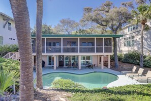 A two-story building with a pool, surrounded by palm trees and other vegetation.