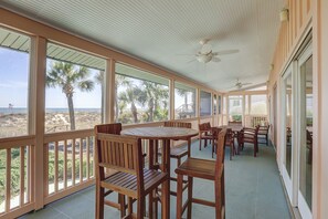 Un espacio al aire libre cubierto con mobiliario de madera y grandes ventanales con vistas a la playa.