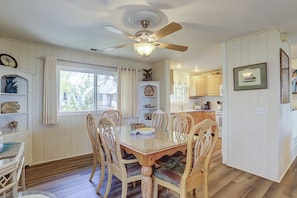A dining area with a wooden table and chairs, a ceiling fan, and a view of the kitchen.
