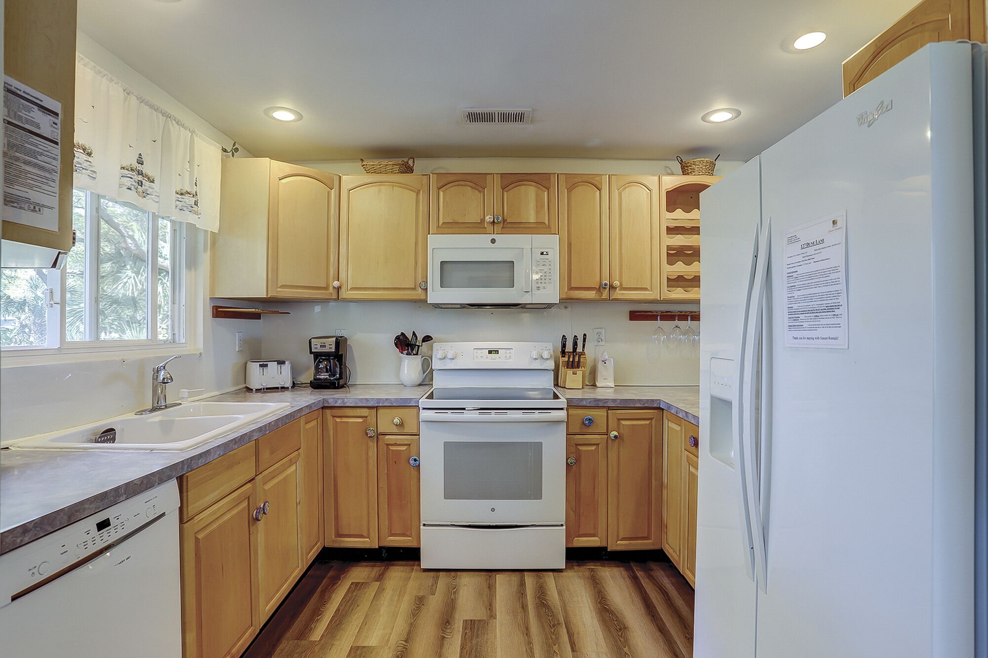 A kitchen with wooden cabinets, a microwave, an oven, a refrigerator, and a window with curtains.