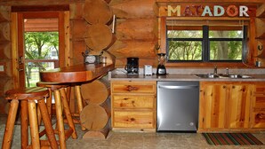 Une cuisine rustique avec des meubles en bois, un lave-vaisselle en acier inoxydable et un coin bar avec des tabourets.