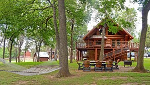 Une cabane en bois dotée d’un balcon, entourée d’arbres et agrémentée d’un hamac.