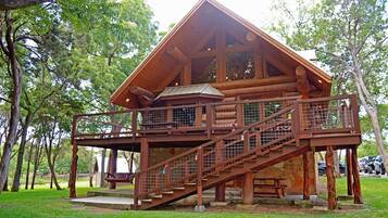A rustic cabin with a wooden exterior, a stone foundation, and a wooden staircase leading to a deck.