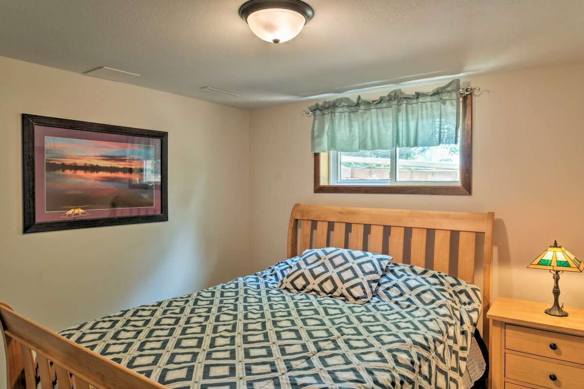 A bedroom with a bed, a nightstand, a lamp, a window with curtains, and a framed picture on the wall.