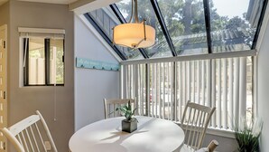 Spiseplads med et rundt bord, stole, en hængende lampe og udsigt gennem store vinduer.