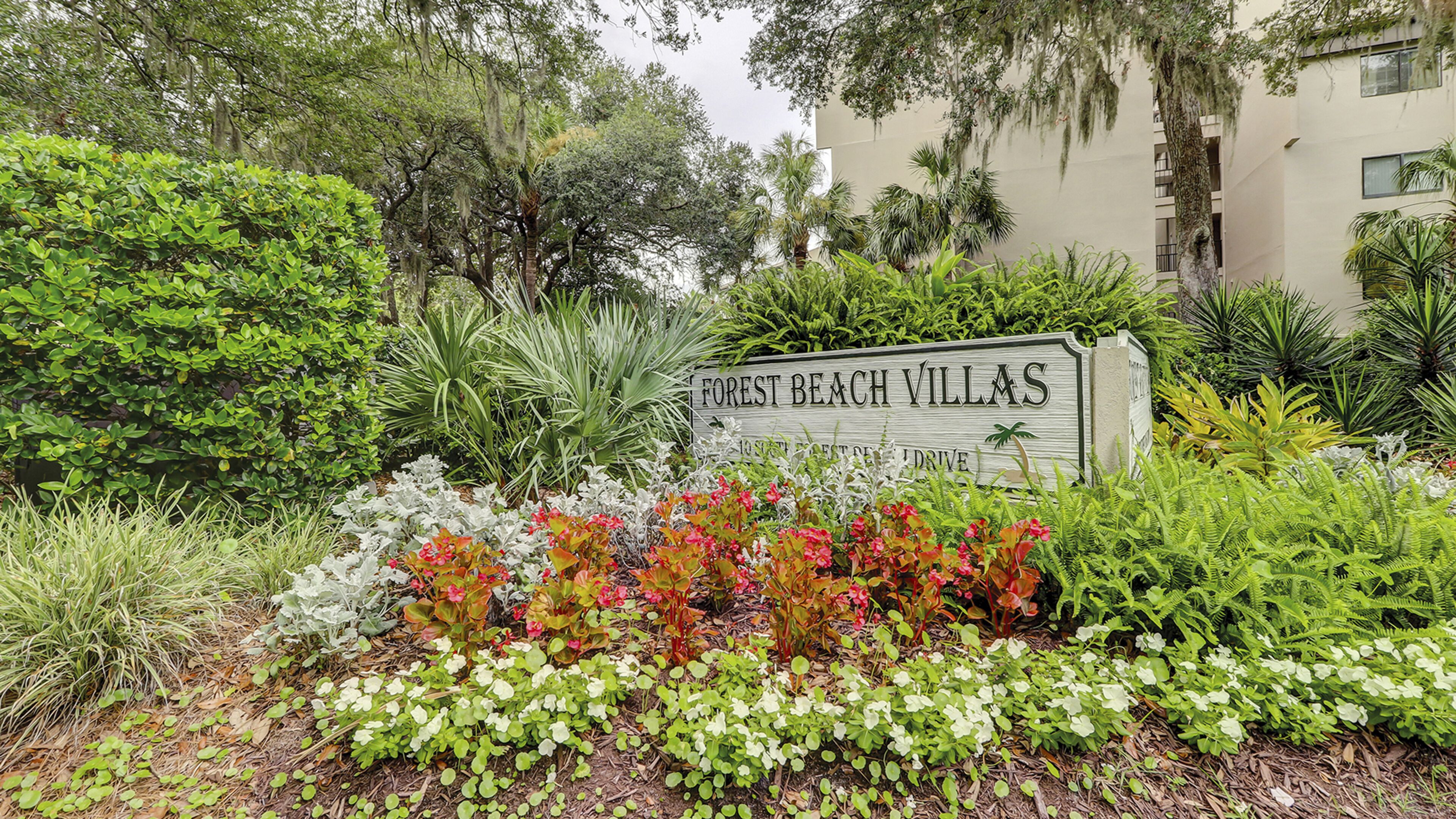 Un letrero de Forest Beach Villas con un exuberante jardín al frente.