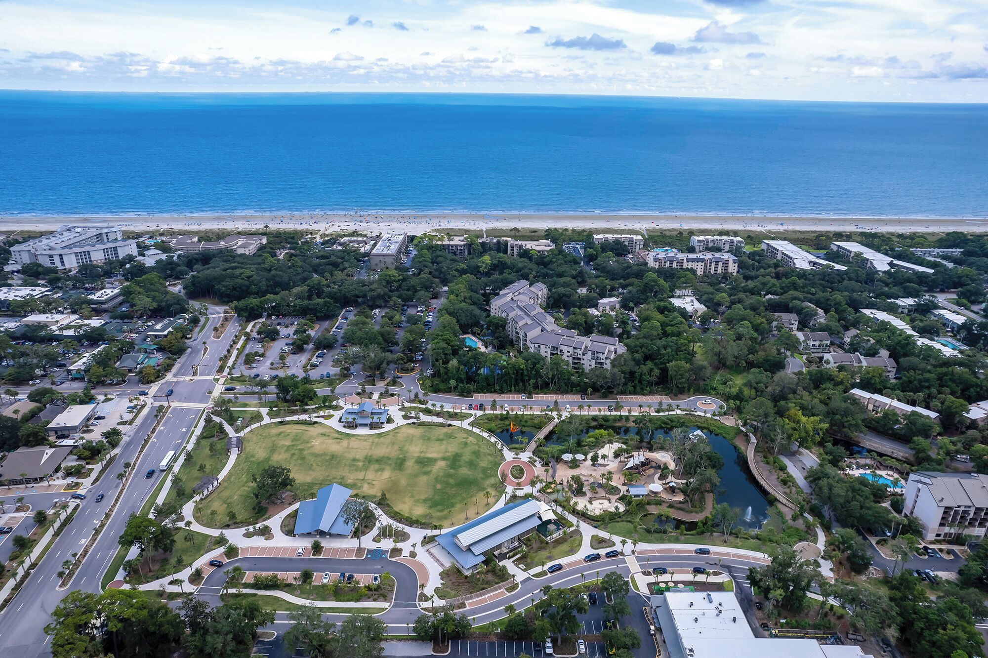 Luftaufnahme einer Küstenlandschaft mit einem großen Park, einem Jachthafen und Wohngebäuden.