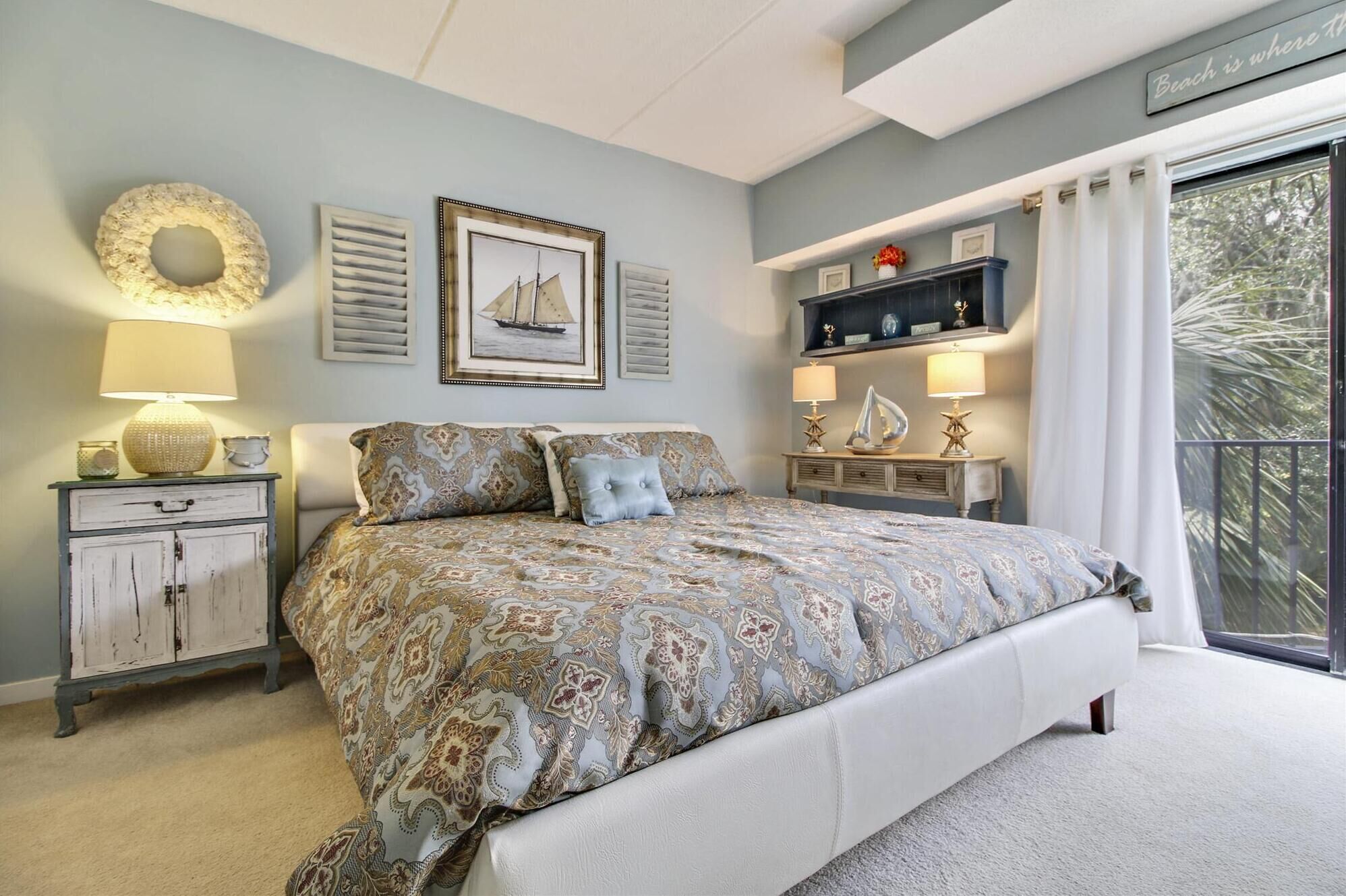 A bedroom with a large bed, a nightstand, a dresser, a wall-mounted shelf, and a window with curtains.