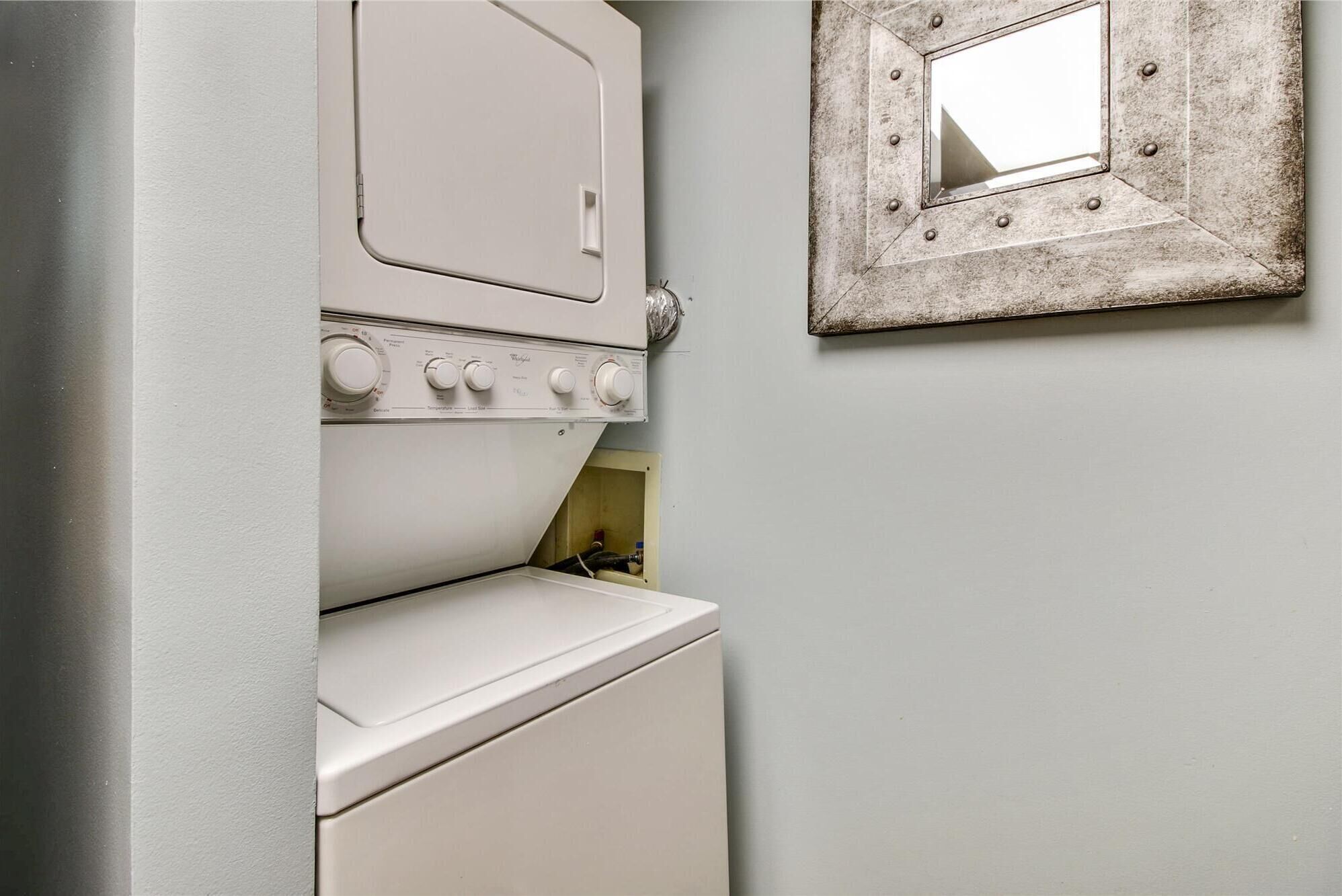 A laundry room with a washing machine and dryer, a mirror on the wall, and a door leading to another room.