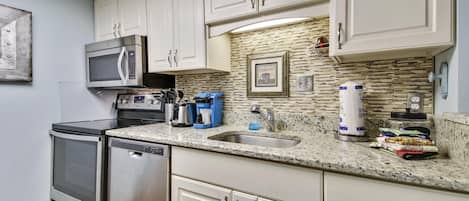 A kitchen with white cabinets, a granite countertop, a microwave, a stove, and a dishwasher.