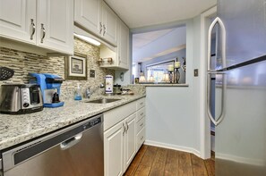 A kitchen with white cabinets, a granite countertop, a coffee maker, a dishwasher, and a refrigerator.