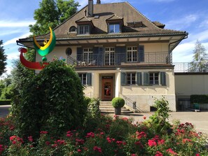 A two-story house with a balcony, a front door, and a staircase leading to the entrance.
