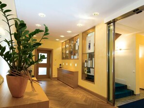 A modern hotel lobby with a wooden floor, a potted plant, a glass door, and a mirrored wall.