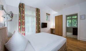 A hotel room with a large bed, a television, a wardrobe, and a view of the outdoors.