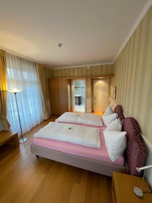 A hotel room with a bed, bedside tables, a lamp, curtains, and a view of the hallway.