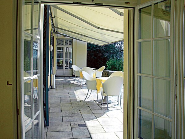 An open patio with a table and chairs, a covered area, and a view of greenery.