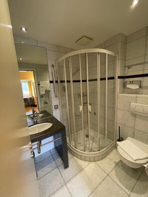 A modern bathroom with a curved glass shower enclosure, a vanity with a sink, and a toilet.