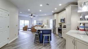 Une cuisine moderne dotée d’un îlot central, d’appareils électroménagers en acier inoxydable et d’un ventilateur de plafond.
