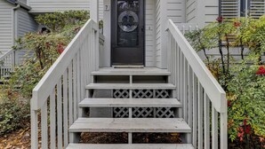 Une vue de face d’une maison avec une porte d’entrée noire, des marches blanches et une rambarde blanche.