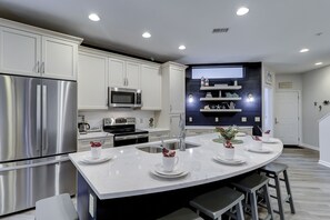 A modern kitchen with stainless steel appliances, a central island with stools, and built-in shelves. - Sunset Rentals | Ocean Breeze 7 | Dog Friendly (Hilton Head)