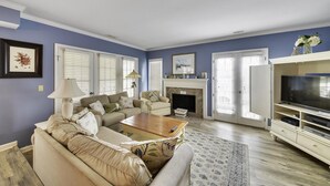 A living room with a sofa set, a coffee table, a fireplace, and a television on a stand. - Sunset Rentals | Evian 164 (Hilton Head)