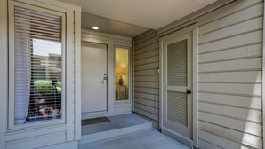 A house entrance with a front door, a small porch, and a window with blinds. - Sunset Rentals | St. Andrews 1772 | Dog Friendly (Hilton Head)