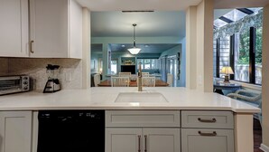 A modern kitchen with white cabinetry, a built-in dishwasher, and a central island with a sink. - Sunset Rentals | St. Andrews 1772 | Dog Friendly (Hilton Head)