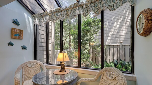 A room with a glass table and wicker chairs, a lamp, and a view of greenery outside. - Sunset Rentals | St. Andrews 1772 | Dog Friendly (Hilton Head)