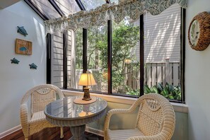 A room with a glass table and wicker chairs, a lamp, and a view of greenery outside. - Sunset Rentals | St. Andrews 1772 | Dog Friendly (Hilton Head)