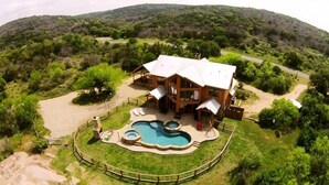 A large wooden house with a swimming pool and hot tubs, surrounded by a fenced yard and lush greenery. - Spacious 5BR Retreat w/ Pool, Hot Tub & Game Room (Burnet)
