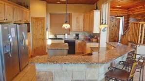 A kitchen with granite countertops, a stone island, wooden cabinets, and a bar area with metal chairs. - Spacious 5BR Retreat w/ Pool, Hot Tub & Game Room (Burnet)