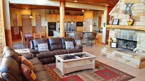 A spacious living room with a leather sofa, a coffee table, and a stone fireplace. - Spacious 5BR Retreat w/ Pool, Hot Tub & Game Room (Burnet)