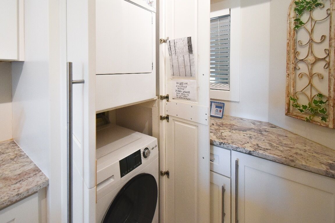 A compact laundry room with a washing machine, a drying rack, and a door with a warning sign.