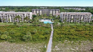 Ein Resort mit mehreren Gebäuden, einem zentralen Poolbereich und einem von Grünpflanzen gesäumten Weg zum Pool.