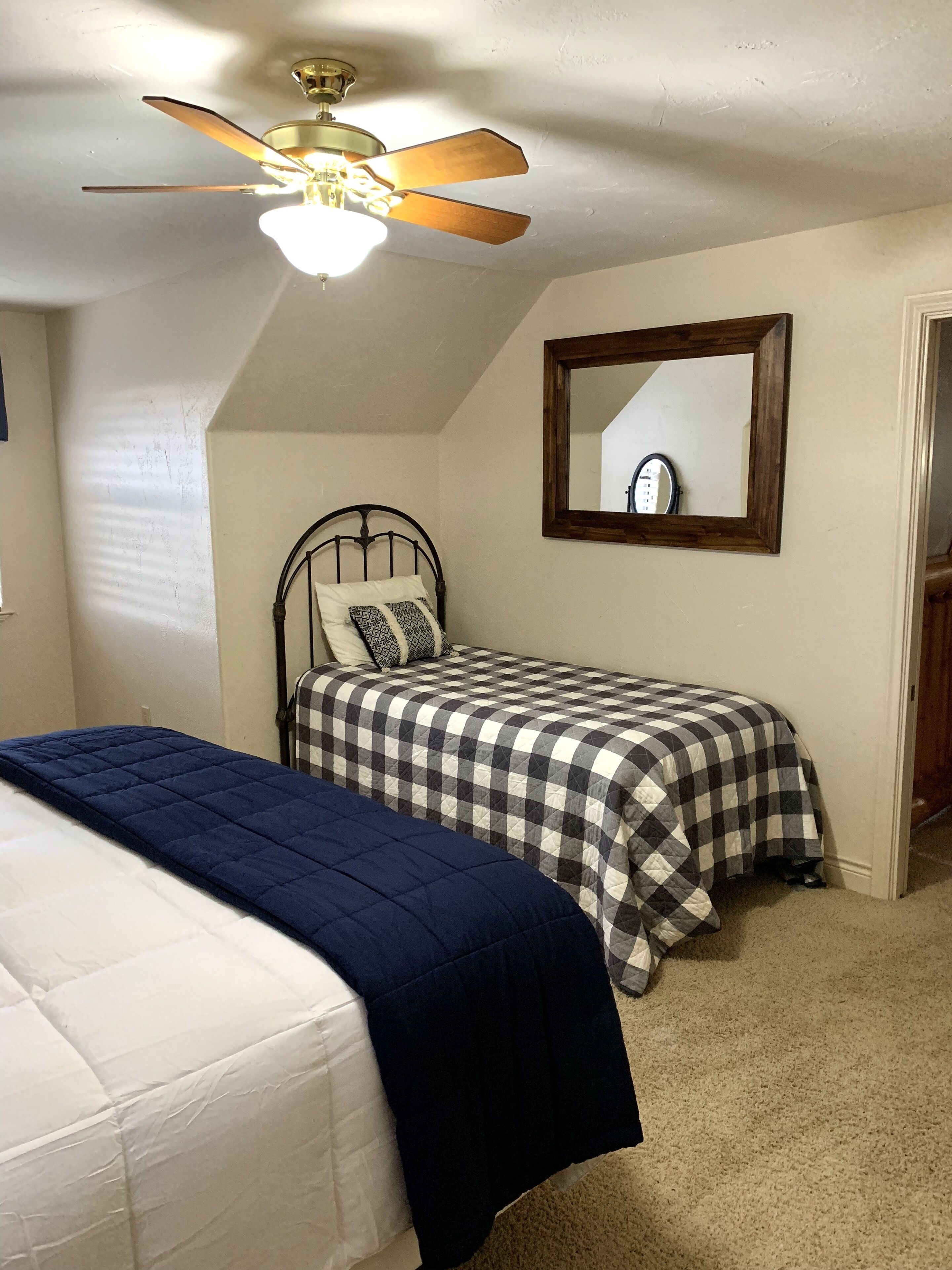 A bedroom with two beds, a ceiling fan, a mirror, and a carpeted floor.