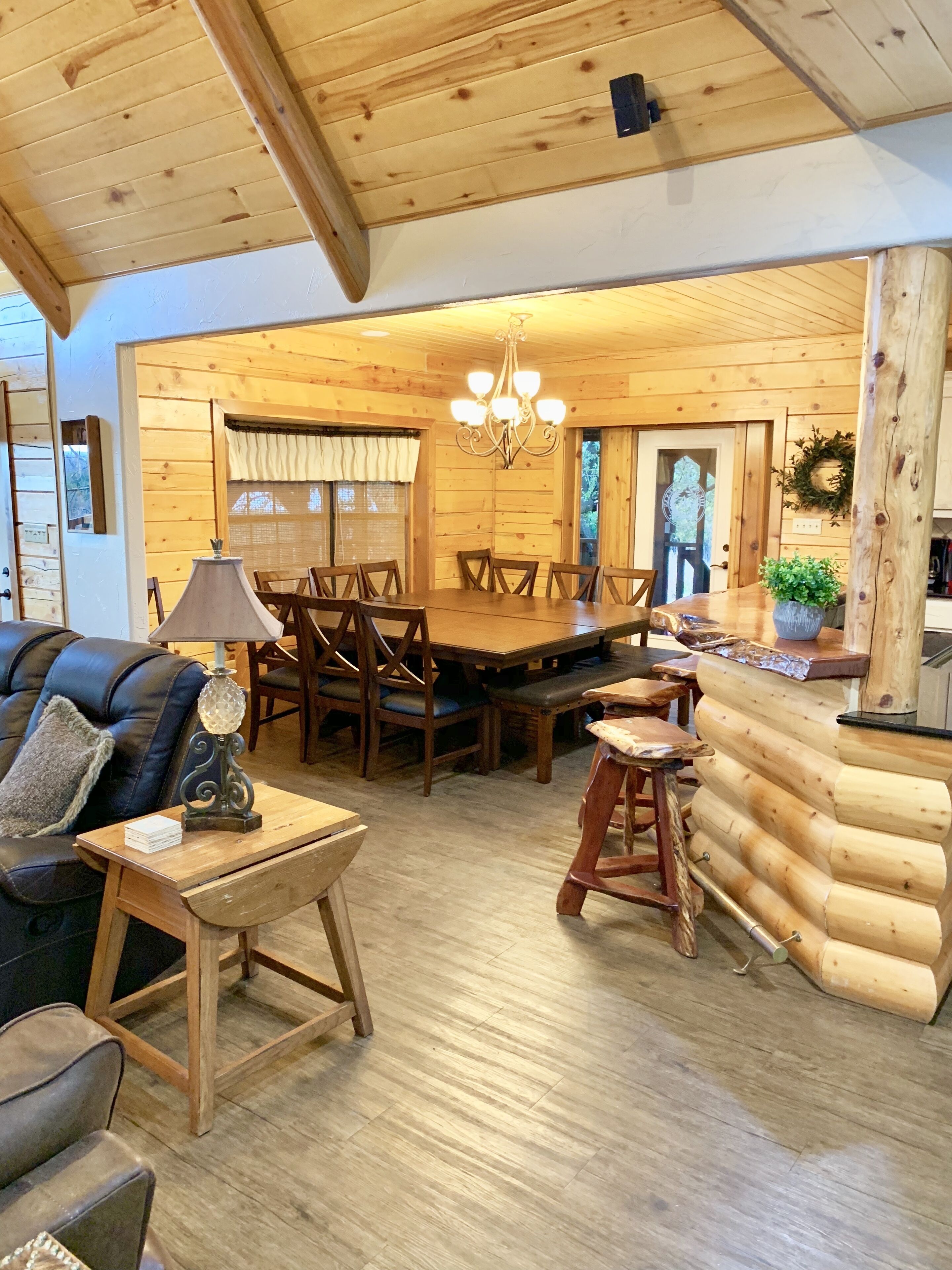 A cozy log cabin interior with a dining area, wooden furniture, and a chandelier.