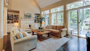 A spacious living room with a high ceiling, large windows, a fireplace, and a cozy seating area. - Sunset Rentals | Mooring Buoy 179 (Hilton Head Island)