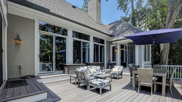 A covered outdoor deck with furniture and a table, large windows, and a chimney. - Sunset Rentals | Mooring Buoy 179 (Hilton Head Island)
