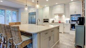 A modern kitchen with white cabinetry, a large island, stainless steel appliances, and wicker chairs. - Sunset Rentals | Mooring Buoy 179 (Hilton Head Island)