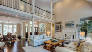 A spacious living area with a high ceiling, a staircase, and a large bookshelf. - Sunset Rentals | Mooring Buoy 179 (Hilton Head Island)