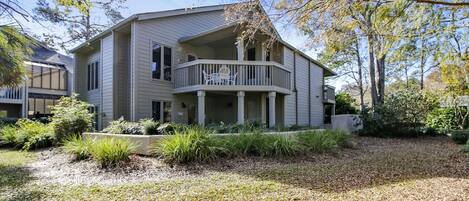 A two-story house with a balcony, surrounded by a well-maintained garden and a gravel driveway.