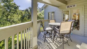 A covered porch with a table and chairs, a sign reading "BEACH", and a view of greenery and a house. - Sunset Rentals | St. Andrews 1876 | Dog Friendly (Hilton Head Island)
