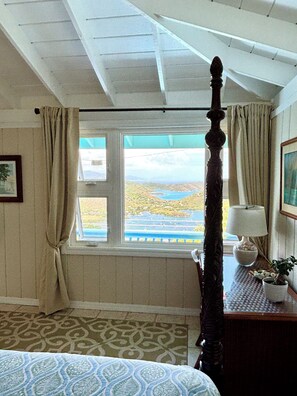 A room with a bed, a window with a view of a landscape, a lamp, and a plant. - Beautiful Cottage w/Stunning View, Tesla Backup Power, Hot Tub, Family or Couple (St. John)