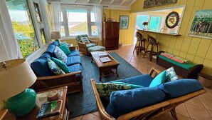 A cozy living room with a sofa, chairs, a coffee table, and a dining area with a bar stool. - Beautiful Cottage w/Stunning View, Tesla Backup Power, Hot Tub, Family or Couple (St. John)