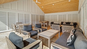 A spacious room with a high wooden ceiling, built-in ceiling fans, and a large window with blinds. There are multiple seating areas with sofas and chairs. - Sunset Rentals | Captains Walk 416 (Hilton Head)