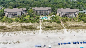 A beachfront hotel with multiple buildings, a swimming pool, and beach umbrellas. - Sunset Rentals | Captains Walk 416 (Hilton Head)