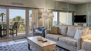 A living room with a sofa, a coffee table, and a TV. There is a balcony with a view of the ocean. - Sunset Rentals | Captains Walk 416 (Hilton Head)